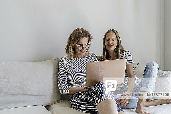Lesbian couple using laptop sitting on sofa at home