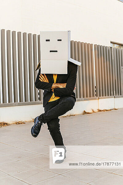 Man wearing box with face standing with arms crossed on footpath