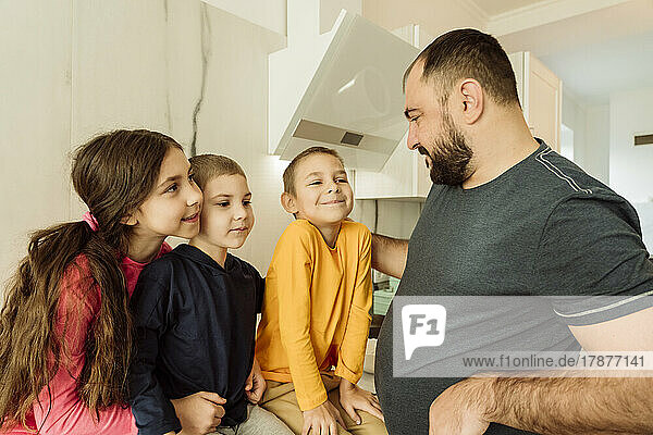 Smiling father talking with children in kitchen