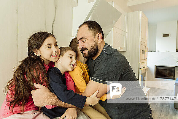 Smiling father embracing children in kitchen