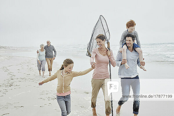 Carefree family with daughter walking on the beach grandparents following in background