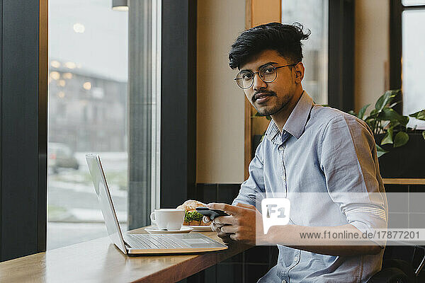 Freelancer with smart phone and laptop sitting in cafe