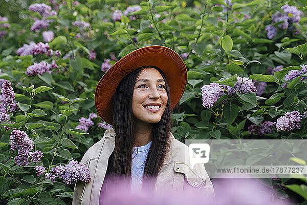 Lächelnde Frau mit Hut inmitten von Blüten im Park