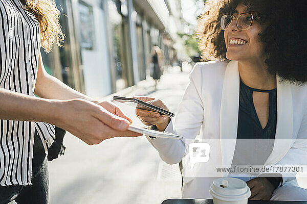 Young businesswoman paying through smart phone at sidewalk cafe