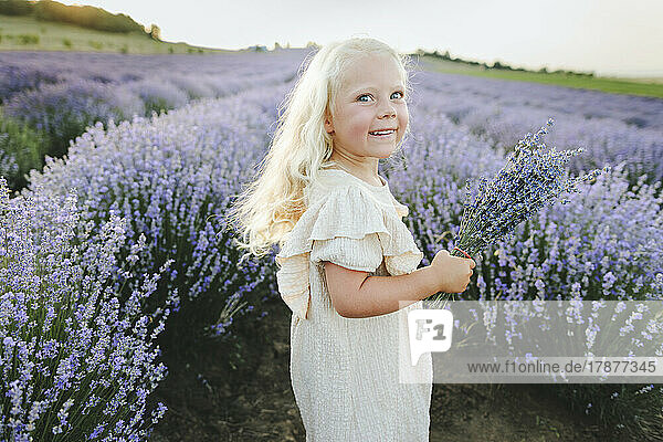 Happy girl with bunch of lavender flowers standing in field