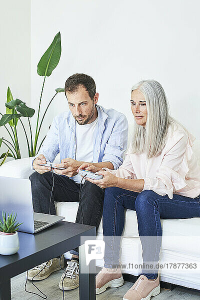 Mother and son playing video game on laptop at home