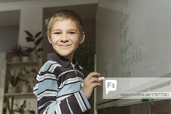 Lächelnder Junge mit Filzstift am Whiteboard zu Hause