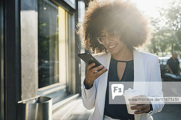Smiling businesswoman with coffee cup using mobile phone