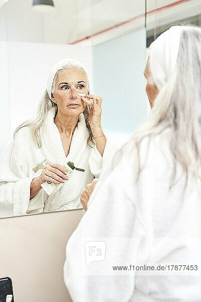 Frau trägt Gesichtscreme auf und schaut in den Spiegel im Badezimmer