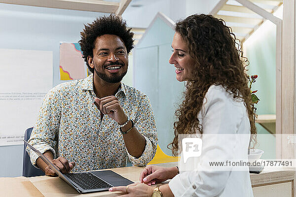 Smiling businessman and businesswoman sharing laptop in office