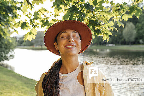 Glückliche Frau mit Hut und geschlossenen Augen im Park