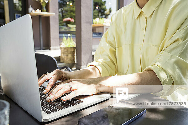 Hands of freelancer using laptop at sidewalk cafe
