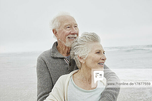 Happy senior couple standing smiling on windy beach