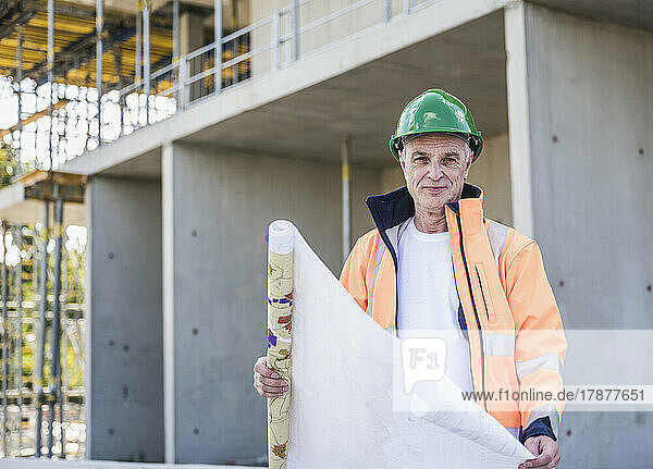 Lächelnder leitender Bauarbeiter mit Bauplan vor Ort