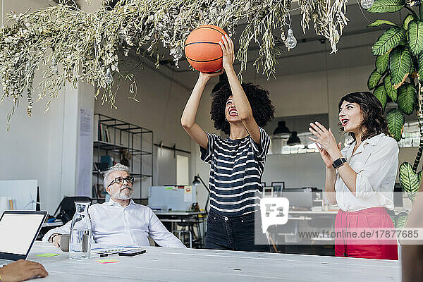 Businesswoman playing basketball by colleague cheering at office