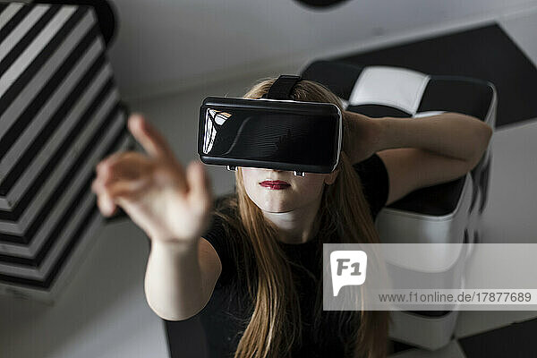 Teenager-Mädchen mit Virtual-Reality-Headset gestikuliert mit erhobener Hand