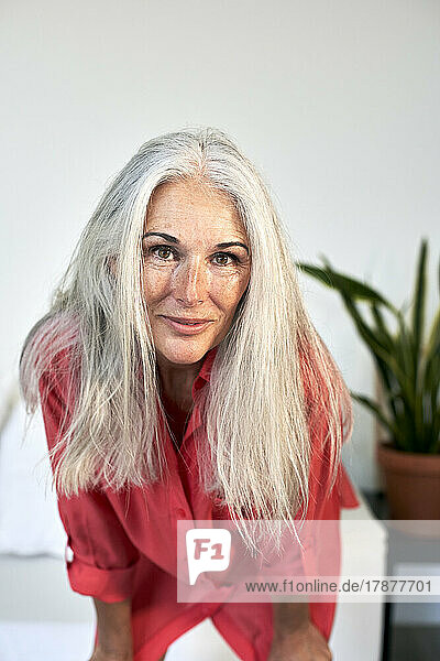 Smiling mature woman with gray hair bending in front of wall