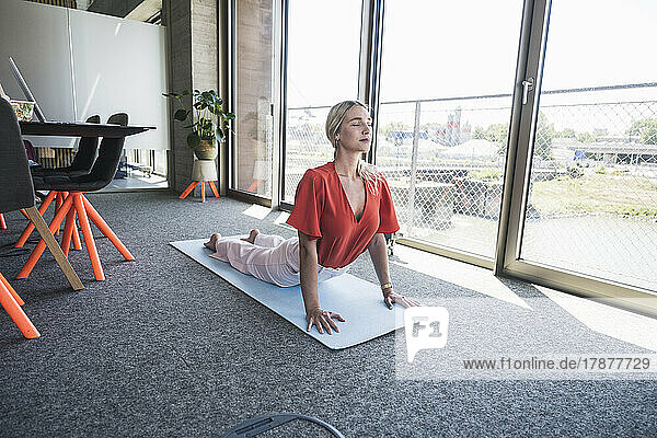 Businesswoman practicing Urdha Mukha Svanasana on exercise mat in office