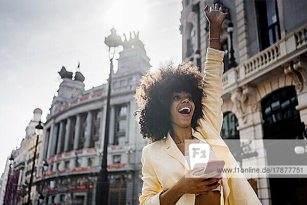 Excited woman with smart phone waving in city