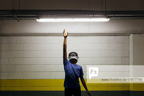 Young man wearing astronaut helmet reaching LED light with hand raised at subway