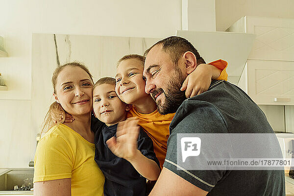 Happy parents embracing sons in kitchen