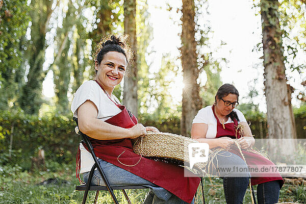 Happy artisan with coworker weaving esparto grass in garden