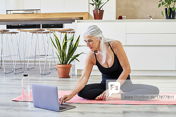 Fitte Frau sitzt zu Hause mit Laptop auf einer Trainingsmatte