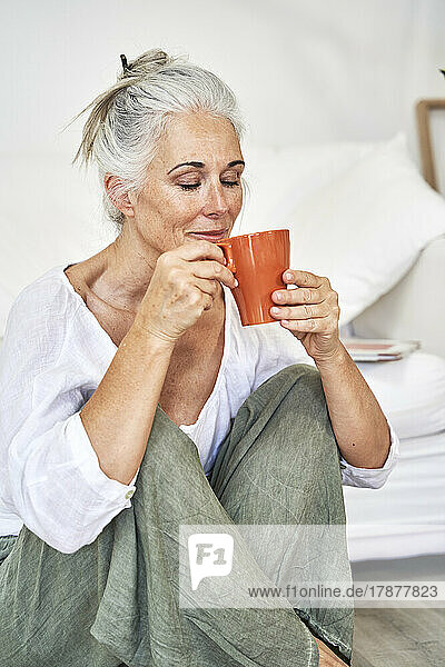 Lächelnde Frau riecht zu Hause Kaffee in der Tasse