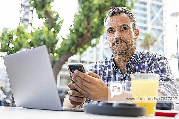 Mature man sitting with laptop and smart phone at sidewalk cafe