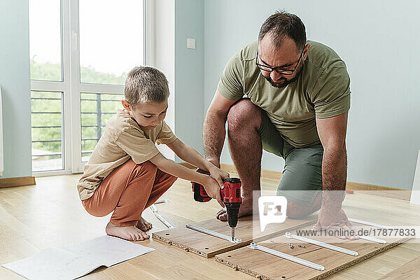 Vater und Sohn benutzen zu Hause Bohrmaschine auf Planke