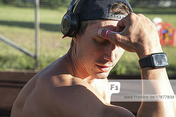 Shirtless athlete wearing smart watch listening music through wireless headphones on sunny day