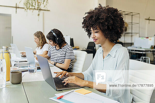 Smiling businesswoman with curly hair working on laptop in office