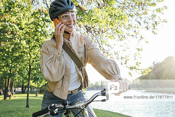 Smiling woman talking on smart phone with bicycle