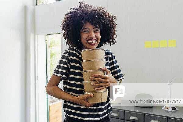 Happy businesswoman holding lunch boxes in office