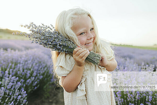 Smiling girl with lavender bouquet standing in field