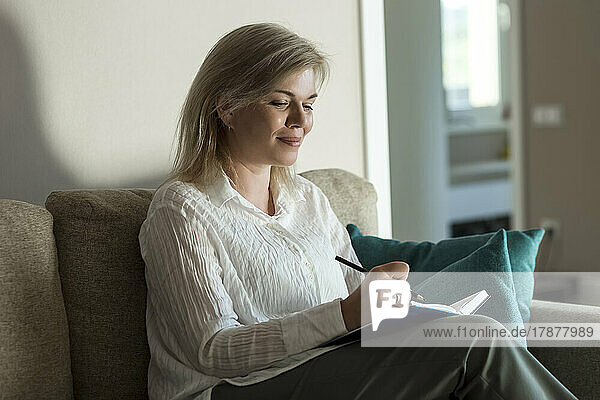 Smiling mature woman writing in diary at home
