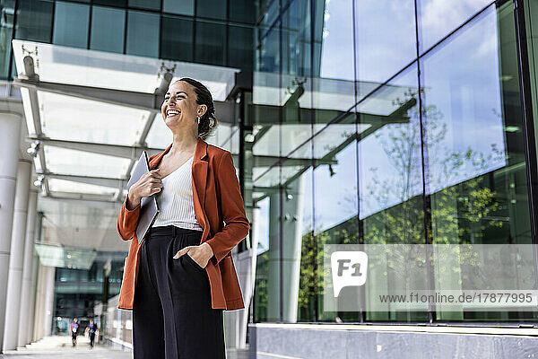 Happy businesswoman holding laptop in front of office building