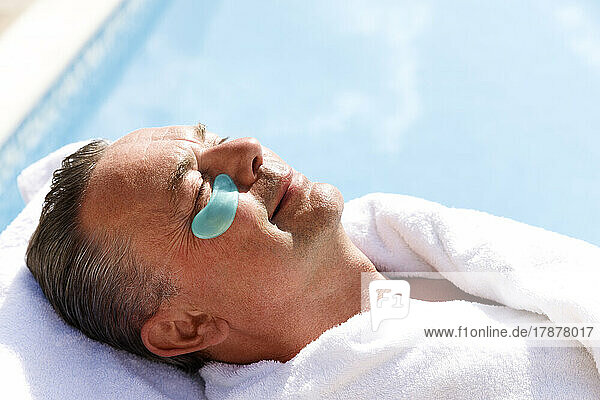 Smiling mature man with collagen patch below eye at pool spa