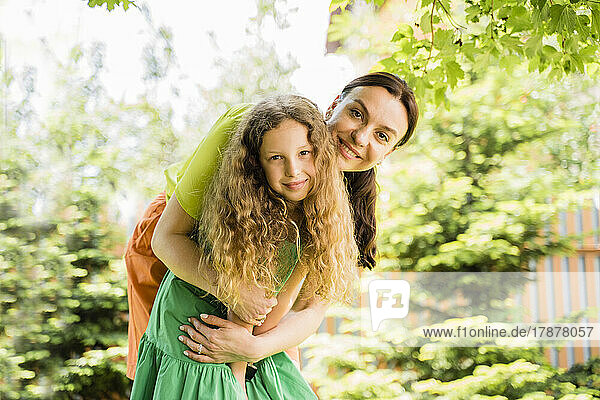 Smiling mother embracing daughter from back at back yard