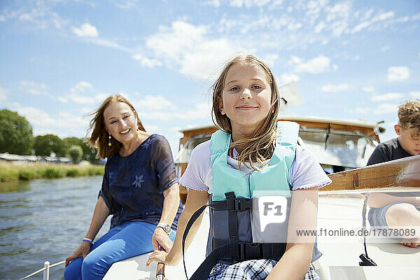 Smiling girl wearing life jacket sitting on boat deck with family at vacation