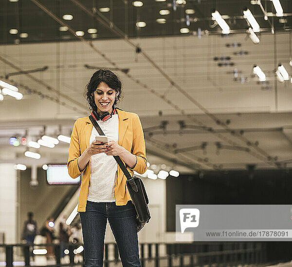 Lächelnde Geschäftsfrau  die an der U-Bahn-Station SMS am Telefon sendet