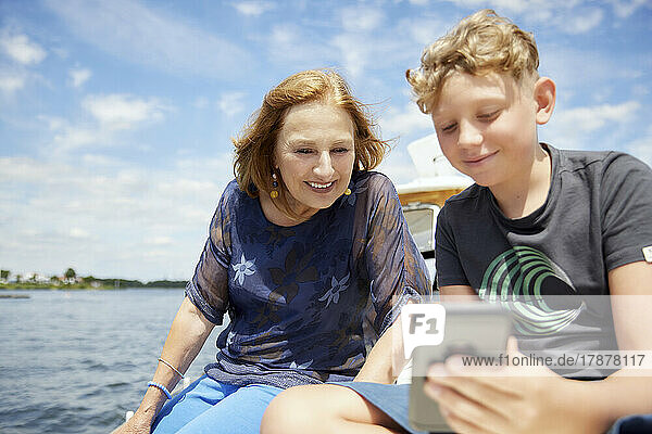 Boy sharing smart phone with grandmother on boat