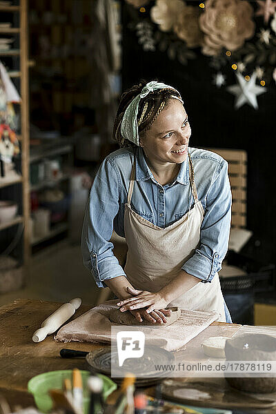Smiling potter kneading clay on workbench at art studio