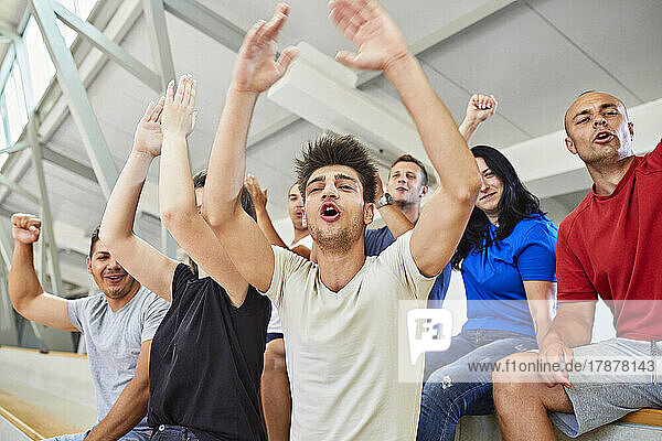 Man with arms raised cheering with friends in stadium