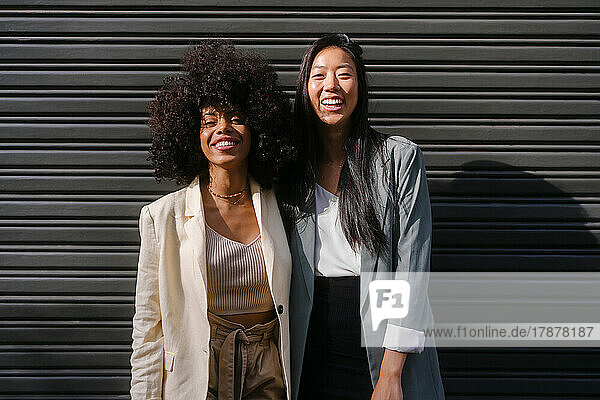 Multiracial friends standing in front of shutter on sunny day