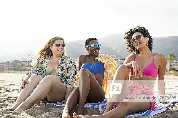 Lächelnde Freunde in Badebekleidung sitzen im Urlaub am Strand