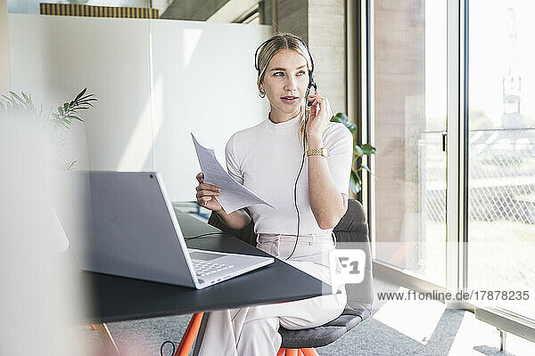 Young customer service representative talking on headset sitting at desk in office
