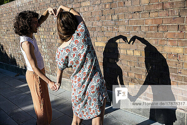 Junges Paar formt an einem sonnigen Tag vor der Wand ein Herz