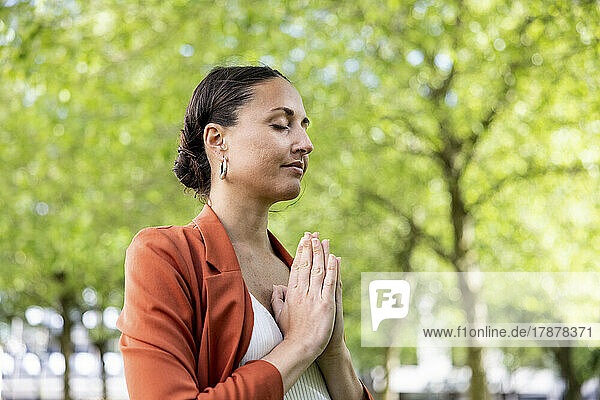 Businesswoman with hands clasped meditating in park