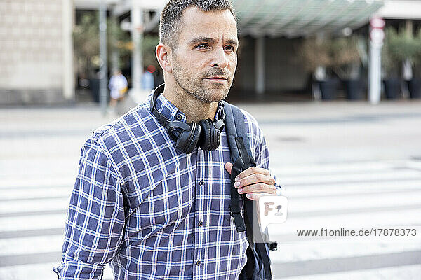 Mature man with wireless headphones and backpack crossing street